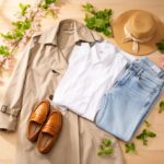 Minimalistyczne ubrania wiosenne: trencz, bluzka, dżinsy, mokasyny, kapelusz i wiosenne liście na drewnie.